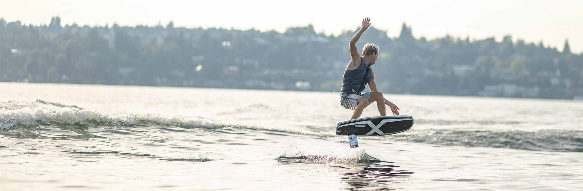 Person wakesurfing on a lake with a distant shoreline in the background.