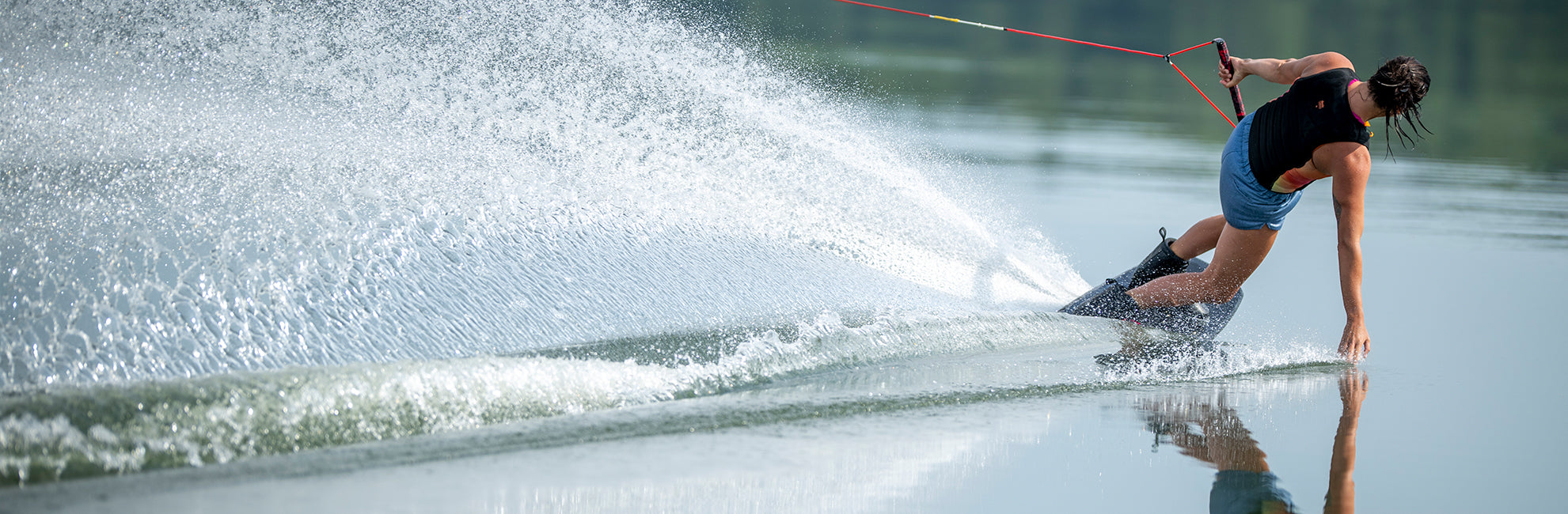 Person waterskiing on a calm lake, creating a large spray of water.