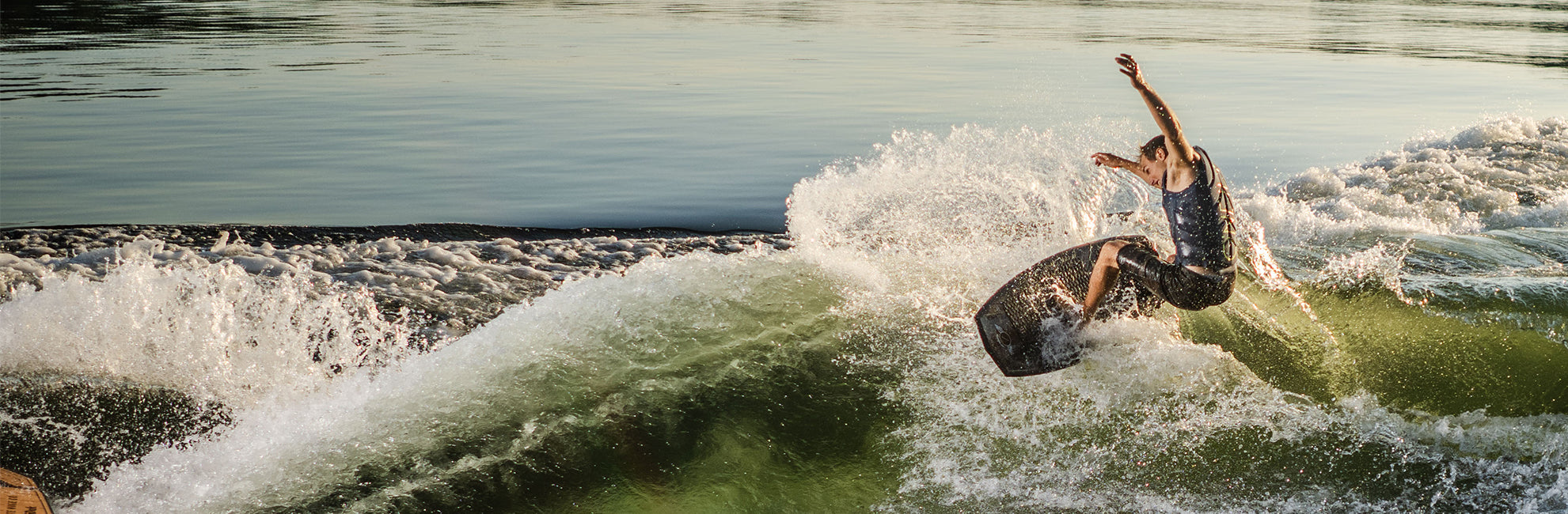 Person surfing on a wave, performing a trick with arms extended under a clear sky.