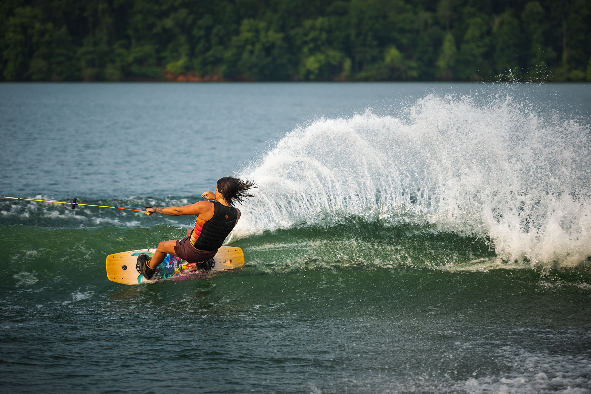 Person wakeboarding on a lake, creating a large splash of water behind them.