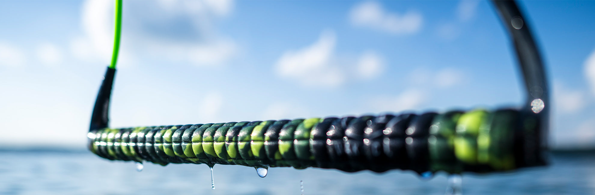 Close-up of a wet rope with droplets, against a blurred blue sky and water backdrop.